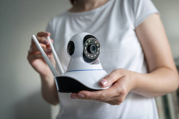 Close up on midsection and hands of unknown caucasian woman holding home security surveillance camera while standing in room adjusting and setting up equipment copy space